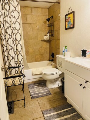 Une salle de bain équipée de toilettes, d’une baignoire, d’un rideau de douche, d’un porte-serviettes et d’une étagère contenant des articles de toilette.