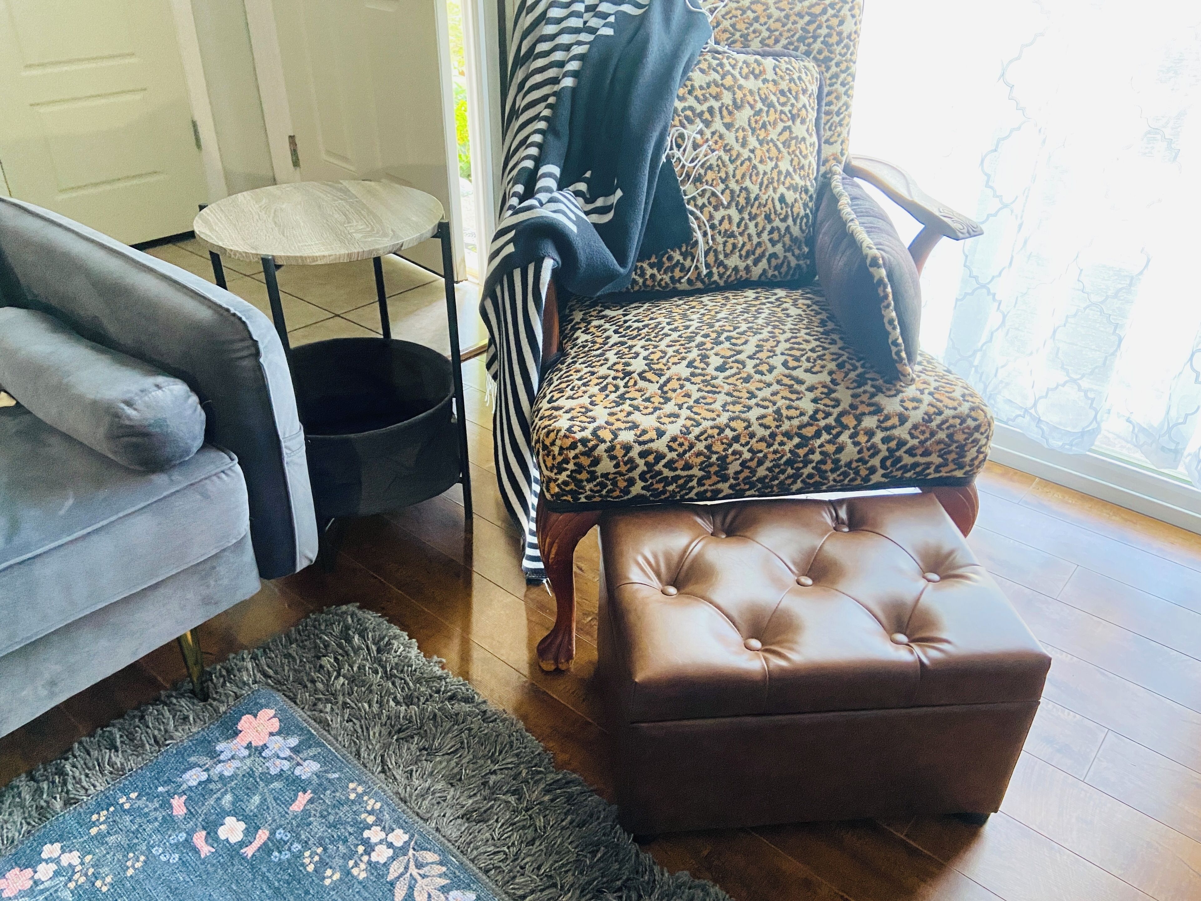 A living room with a grey sofa, a leopard print armchair, a round coffee table, and a brown ottoman.