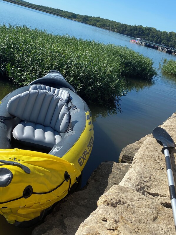 Un radeau et un kayak gonflables près d’une étendue d’eau calme, bordée d’une rive rocheuse et d’une végétation luxuriante.
