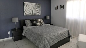 A bedroom with a bed, two bedside tables, a lamp, a wall art piece, and a window with curtains. - Sun, beach, and great savings: huge discounts on holiday destinations! (Cape Coral)
