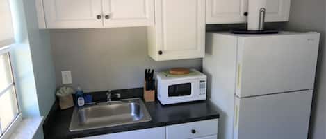A kitchen with white cabinets, a stainless steel sink, a microwave, and a refrigerator.