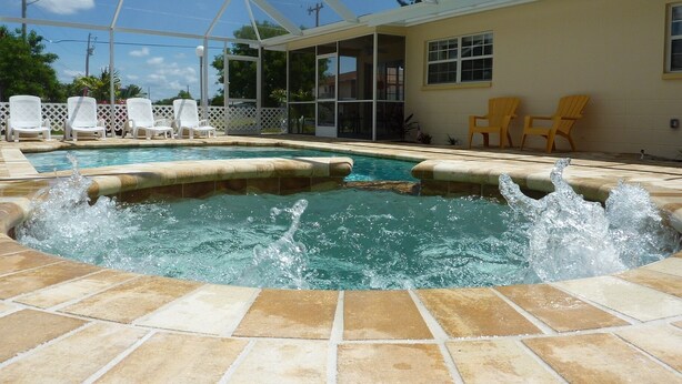 A swimming pool with a hot tub, surrounded by a covered patio area with chairs and a fence. - Sun, beach, and great savings: huge discounts on holiday destinations! (Cape Coral)