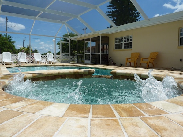 Ein Schwimmbecken mit Whirlpool, umgeben von einer überdachten Terrasse mit Stühlen und einem Zaun.