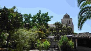 A courtyard with a fountain, surrounded by lush greenery and a historic building with a bell tower.