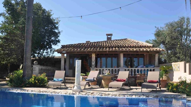 A poolside area with lounge chairs, a pergola, and a building with a tiled roof.