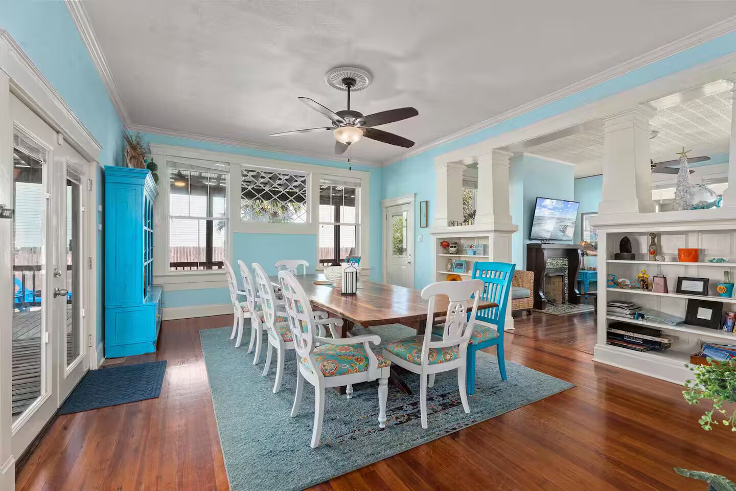 A dining area with a wooden table and chairs, a ceiling fan, and a bookshelf with various items.