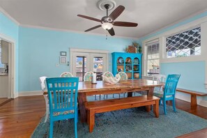 A dining room with a wooden table, blue chairs, a ceiling fan, and a blue cabinet with decorative items.