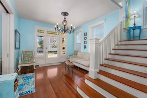 A hallway with a staircase, a chandelier, and a blue wall.