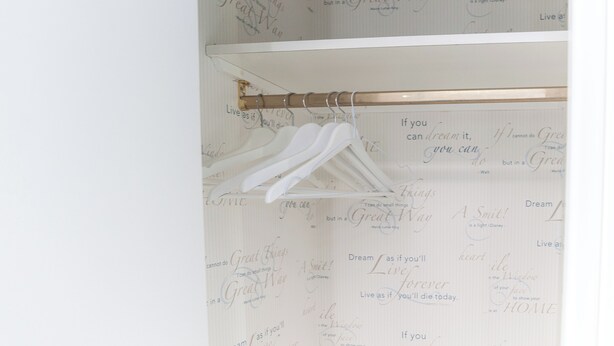 A closet with white hangers and a wooden rod. The wall behind has motivational quotes. - World Wide Bed Prenestino (Rome)