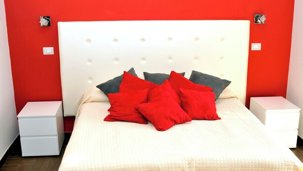 A bed with a white headboard, red and grey pillows, and a white nightstand on each side. - World Wide Bed Prenestino (Rome)