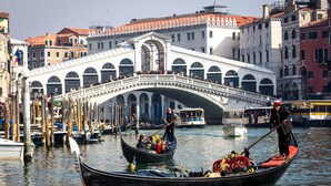 Una góndola con pasajeros y un gondolero en un canal de Venecia, Italia, con el Puente de Rialto al fondo.