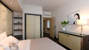 Una habitación de hotel moderna con cama, armario, escritorio, lámpara y un cuadro en la pared.