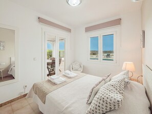 A bedroom with a bed, a chair, a table, and a window with a view.