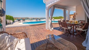 En træterrasse med pool, udendørs møbler og havudsigt.