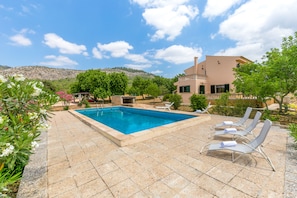 Une piscine avec des chaises longues, une terrasse en pierre et un bâtiment doté d’un balcon.