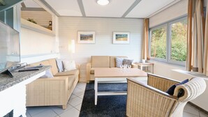 A cozy living room with a sofa, a coffee table, and wicker chairs. There are framed pictures on the wall and a window with curtains. - Ferienhaus 41 in Kirchheim (Kirchheim/Hessen)