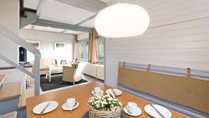 A dining area with a wooden table set for four, a wicker basket with flowers, and a view of the outdoors through a window. - Ferienhaus 41 in Kirchheim (Kirchheim/Hessen)