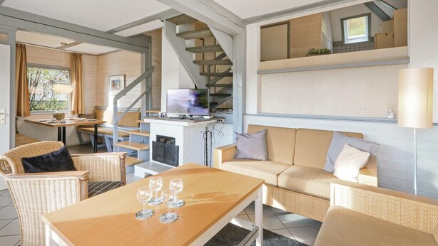 A cozy living area with a sofa, a table with wine glasses, a TV, and a staircase. - Ferienhaus 41 in Kirchheim (Kirchheim/Hessen)