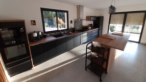 Une cuisine moderne dotée d’une grande fenêtre, d’un four encastré et d’un coin repas avec une table et des chaises en bois.