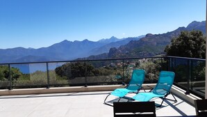 Un balcon avec deux fauteuils bleus, un sol carrelé et une vue sur les montagnes et un lac.