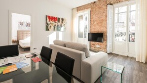 A modern living room with a sofa, a glass coffee table, and a TV mounted on a brick wall.