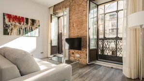A modern living room with a sofa, a glass coffee table, a flat-screen TV, and a large window with a view of the city.