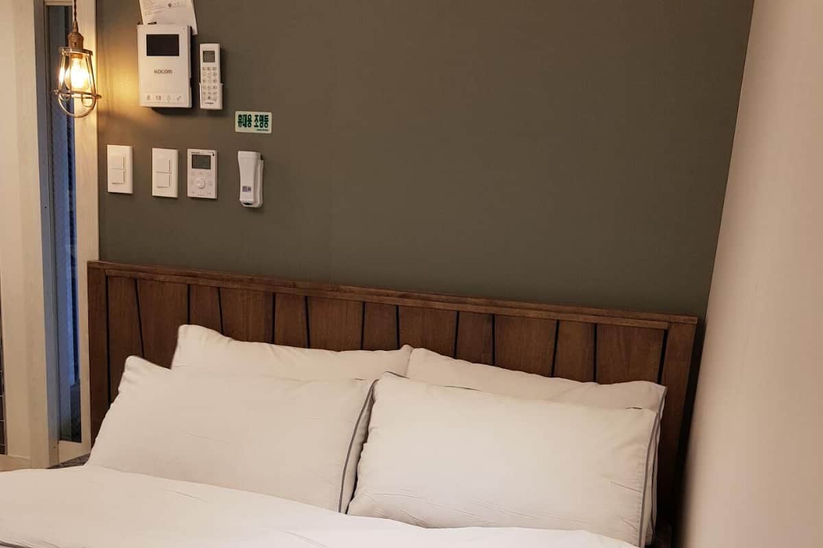 A hotel room with a wooden headboard, white bedding, and a wall-mounted control panel with a thermostat and a phone.