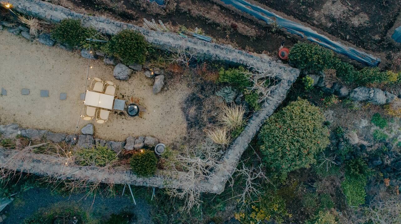 An aerial view of a secluded outdoor area with a stone wall, a table with chairs, and a small circular seating area.
