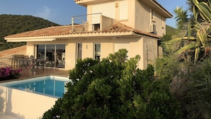 Ein zweistöckiges Haus mit Swimmingpool, Balkon und Blick auf die grüne Umgebung.