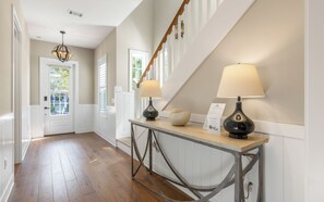 A hallway with a wooden floor, white walls, and a console table with two lamps.