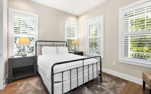 A bedroom with a bed, nightstands, and windows with blinds.