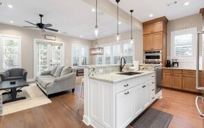 A spacious kitchen with white cabinetry, a central island, and a dining area with a gray sofa and a coffee table. - Sunseeker - Seagrove Home + Pools, Grill & Bikes! (Santa Rosa Beach)