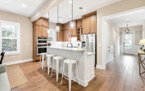 A modern kitchen with wooden cabinets, stainless steel appliances, and a central island with bar stools. - Sunseeker - Seagrove Home + Pools, Grill & Bikes! (Santa Rosa Beach)