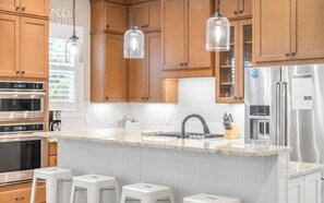 A modern kitchen with wooden cabinets, stainless steel appliances, a marble countertop, and pendant lighting. - Sunseeker - Seagrove Home + Pools, Grill & Bikes! (Santa Rosa Beach)