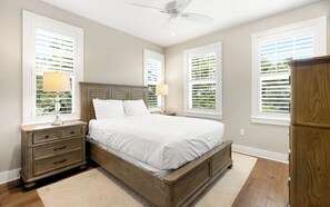 A bedroom with a wooden bed, white bedding, a nightstand with a lamp, and a ceiling fan. - Sunseeker - Seagrove Home + Pools, Grill & Bikes! (Santa Rosa Beach)
