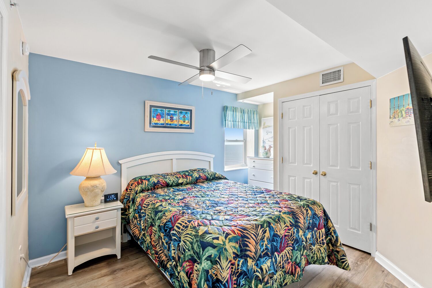 A bedroom with a bed, a nightstand, a lamp, a ceiling fan, and a door.