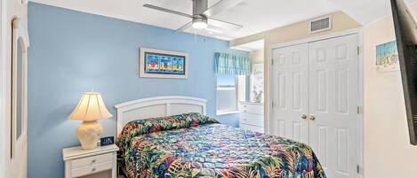 A bedroom with a bed, a nightstand, a lamp, a ceiling fan, and a door.