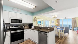 Eine moderne Küche mit Edelstahlgeräten, ein Essbereich mit Meerblick und ein Wohnzimmer mit Balkon.