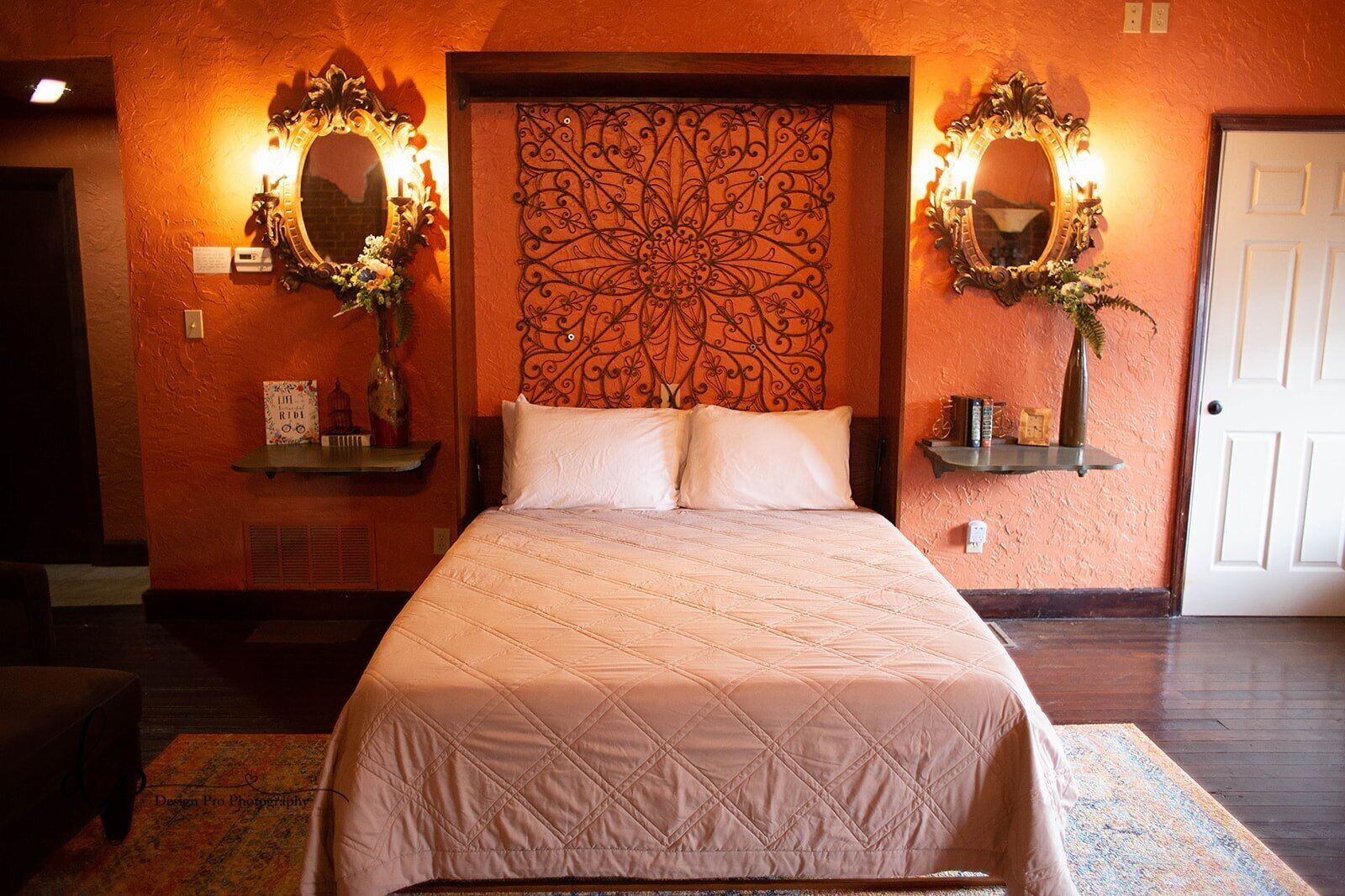 Een hotelkamer met een groot bed, twee wandlampen, een decoratieve hoofdbord en een deur.