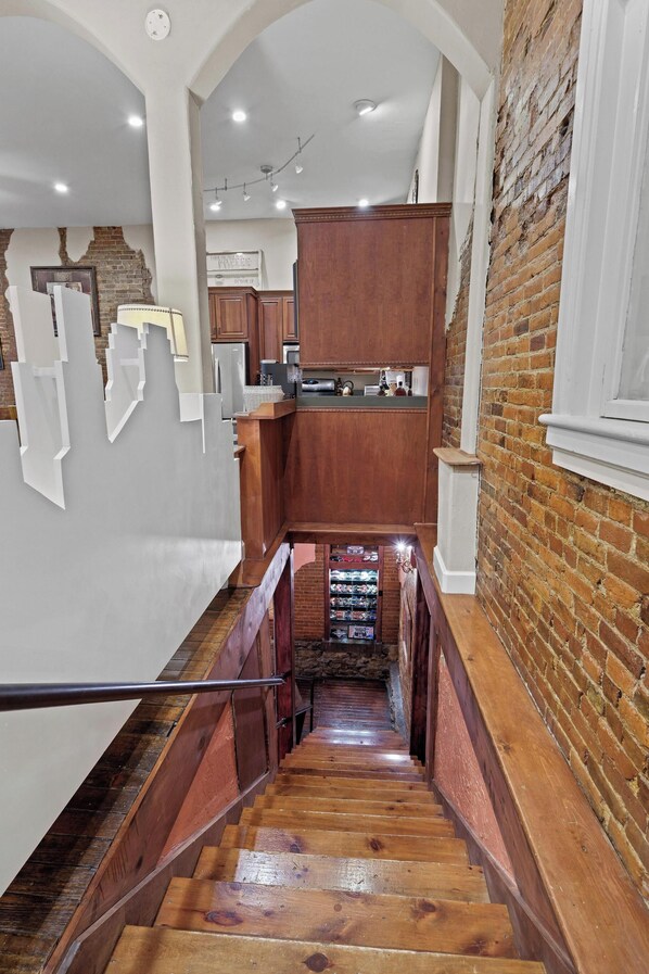A staircase leading to a kitchen area with wooden cabinets and a brick wall.