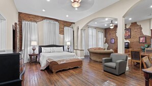 A spacious hotel room with a large bed, a leather ottoman, a gray armchair, and a wooden dining table. - Crossroads Loft:  Steps from Rt. 66 & Carthage Square (Carthage)