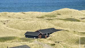 Ein Haus mit geneigtem Dach, das auf einem grasbewachsenen Hügel mit Blick auf den Ozean liegt.