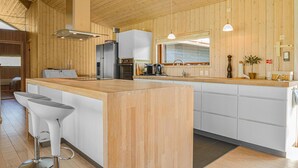 Eine moderne Küche mit Holzvertäfelung, einer zentralen Kochinsel, Barhocker, einem Kühlschrank und einer Spüle.