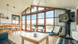 A spacious living area with a large window, a wooden table, and comfortable seating. - Gorgeous home in Løkken with kitchen (Løkken)