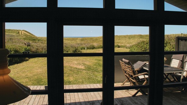 A room with large windows overlooking a grassy landscape and a distant view of the sea. - Gorgeous home in Løkken with kitchen (Løkken)