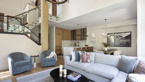 Un salon moderne avec un escalier, un canapé, des fauteuils, une table basse et une cuisine en arrière-plan.