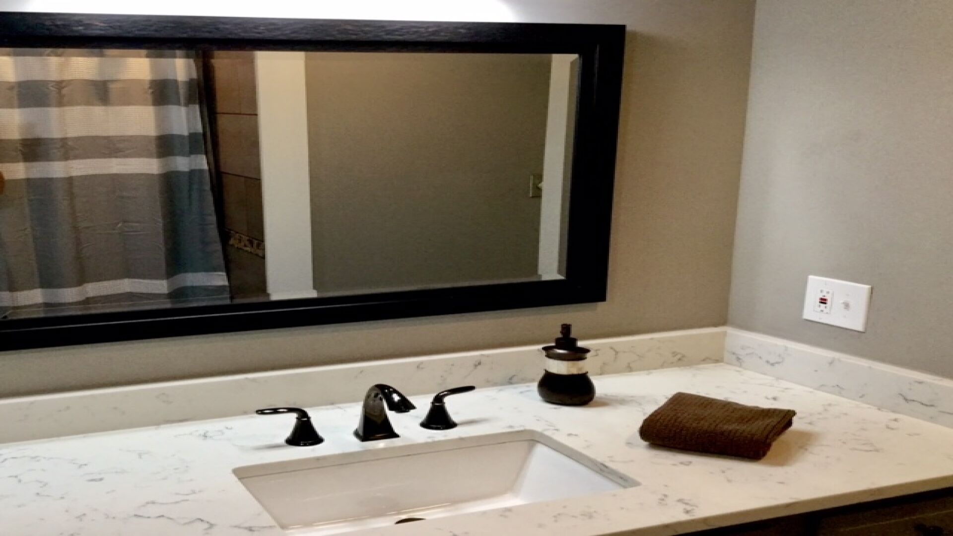 Ein Badezimmer mit einem weißen Marmorwaschbecken, schwarzen Armaturen, einem Seifenspender und einem Handtuch auf der Ablagefläche.