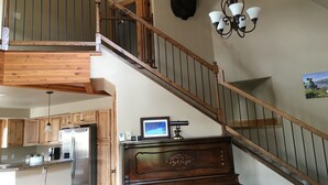 A multi-level home interior with a wooden staircase, a mounted moose head, a chandelier, and a kitchen area. - Yellowstone Archview Guesthouse- Stunning Views For Your Ultimate Family Getaway (Gardiner)