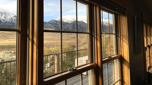 A room with large windows offering a view of snow-capped mountains and a grassy landscape. - Yellowstone Archview Guesthouse- Stunning Views For Your Ultimate Family Getaway (Gardiner)