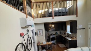 A spacious living area with a high ceiling, a kitchen in the background, and a staircase leading to an upper level. - University Park Garden Guest House (Portland)